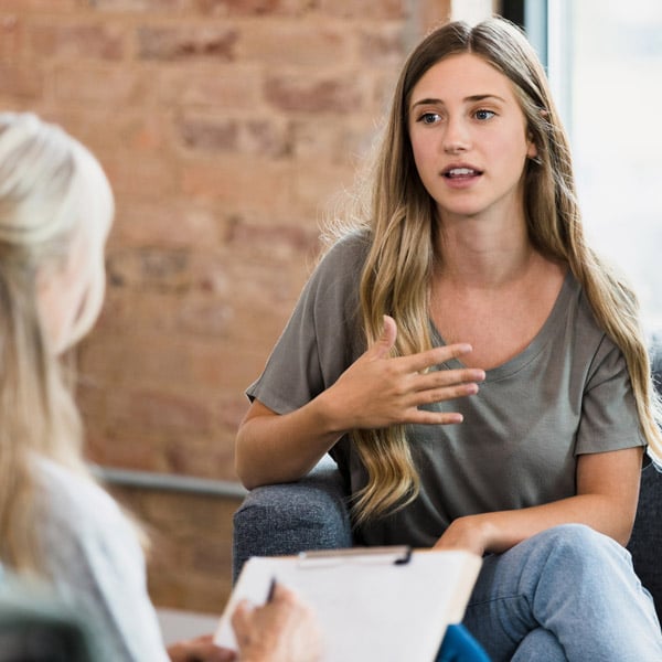 The young adult woman gestures as she talks to the unrecognizable female mature adult counselor.